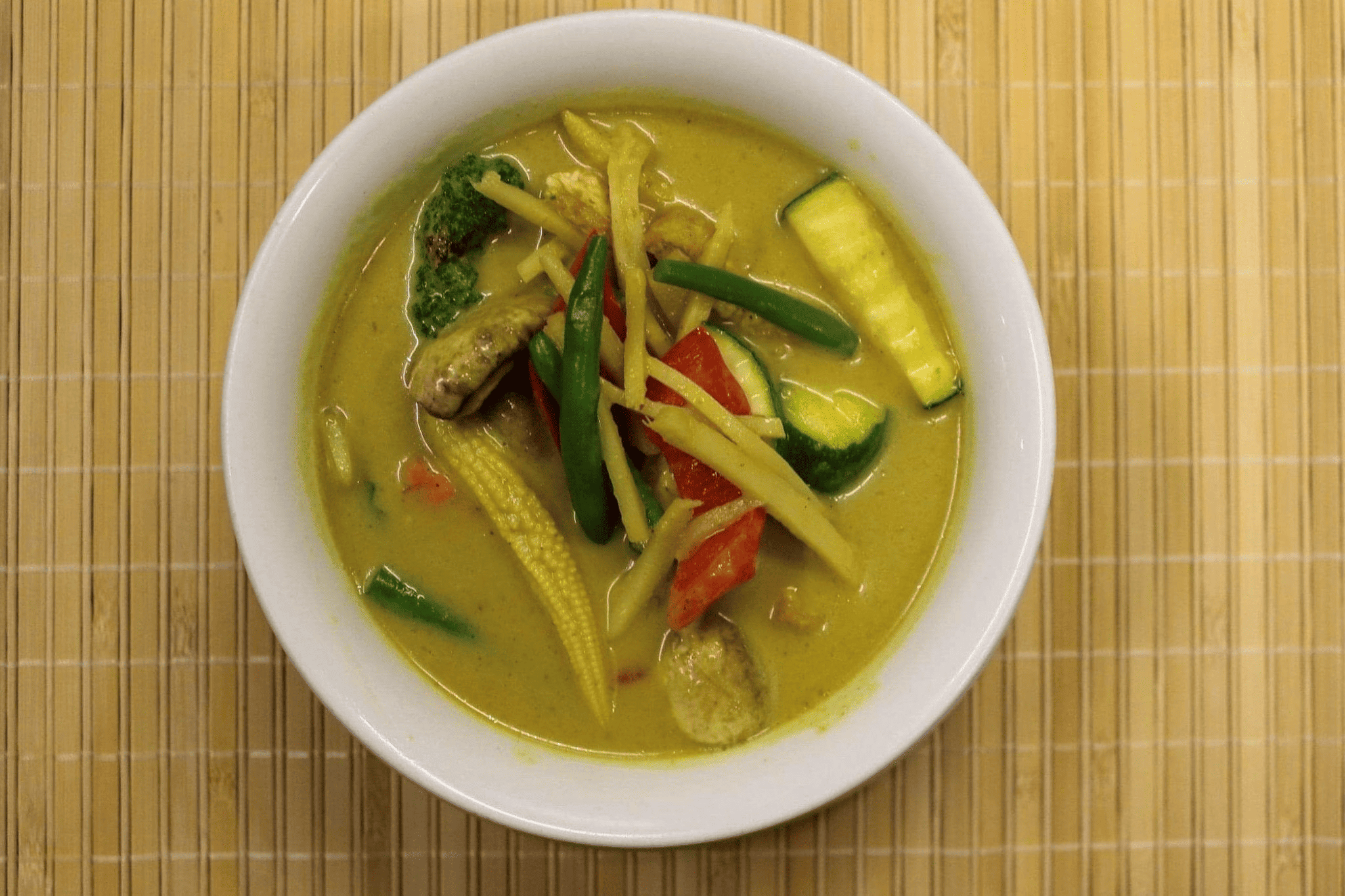 A bowl of Green Curry Chicken with tender meat, vegetables, and aromatic green sauce, garnished with basil.