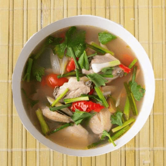 A bowl of Tom Yum Soup, a spicy and sour Thai delicacy, garnished with herbs.