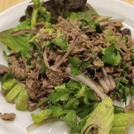 A bowl of Larb: a Thai minced meat salad garnished with herbs and lime wedges.