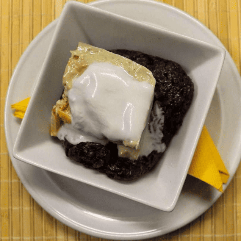 A bowl of black sticky rice topped with a drizzle of coconut milk, exuding sweetness and comfort.